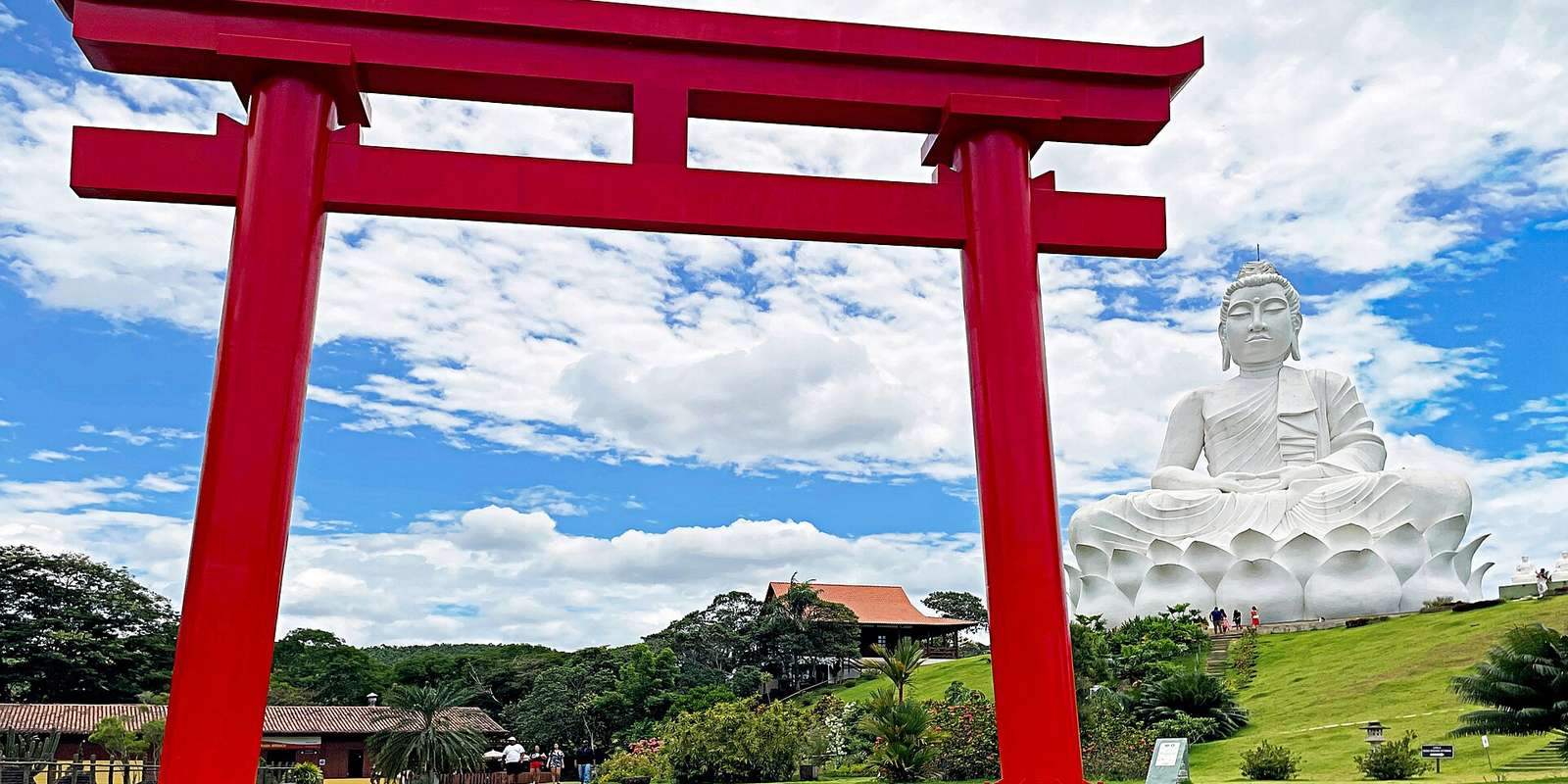 Portal vermelho do Mosteiro Zen Morro da Vargem, em Ibiraçu, e o Buda branco gigante sobre uma colina gramada sob céu azul